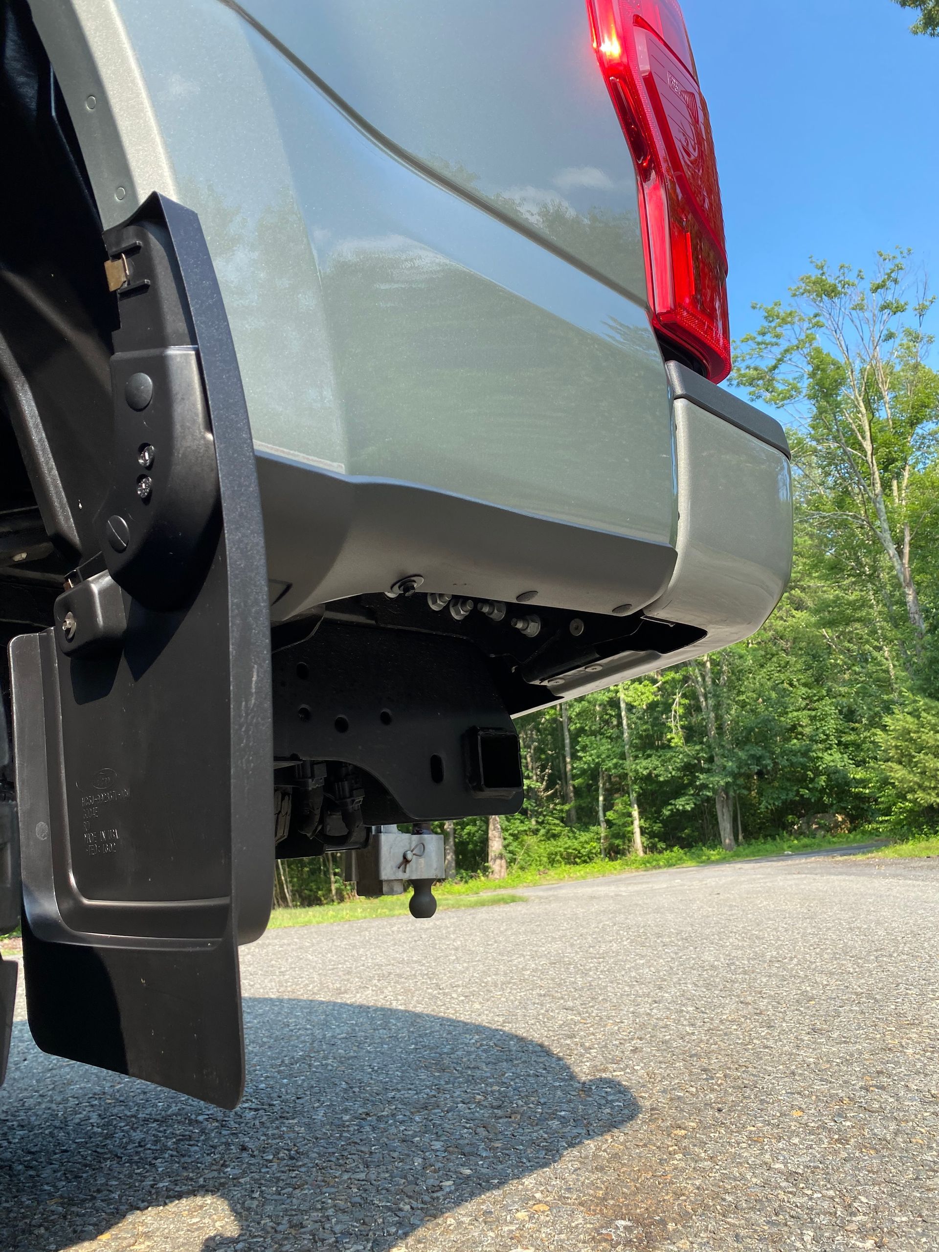 A silver truck with a red tail light is parked on a gravel road.