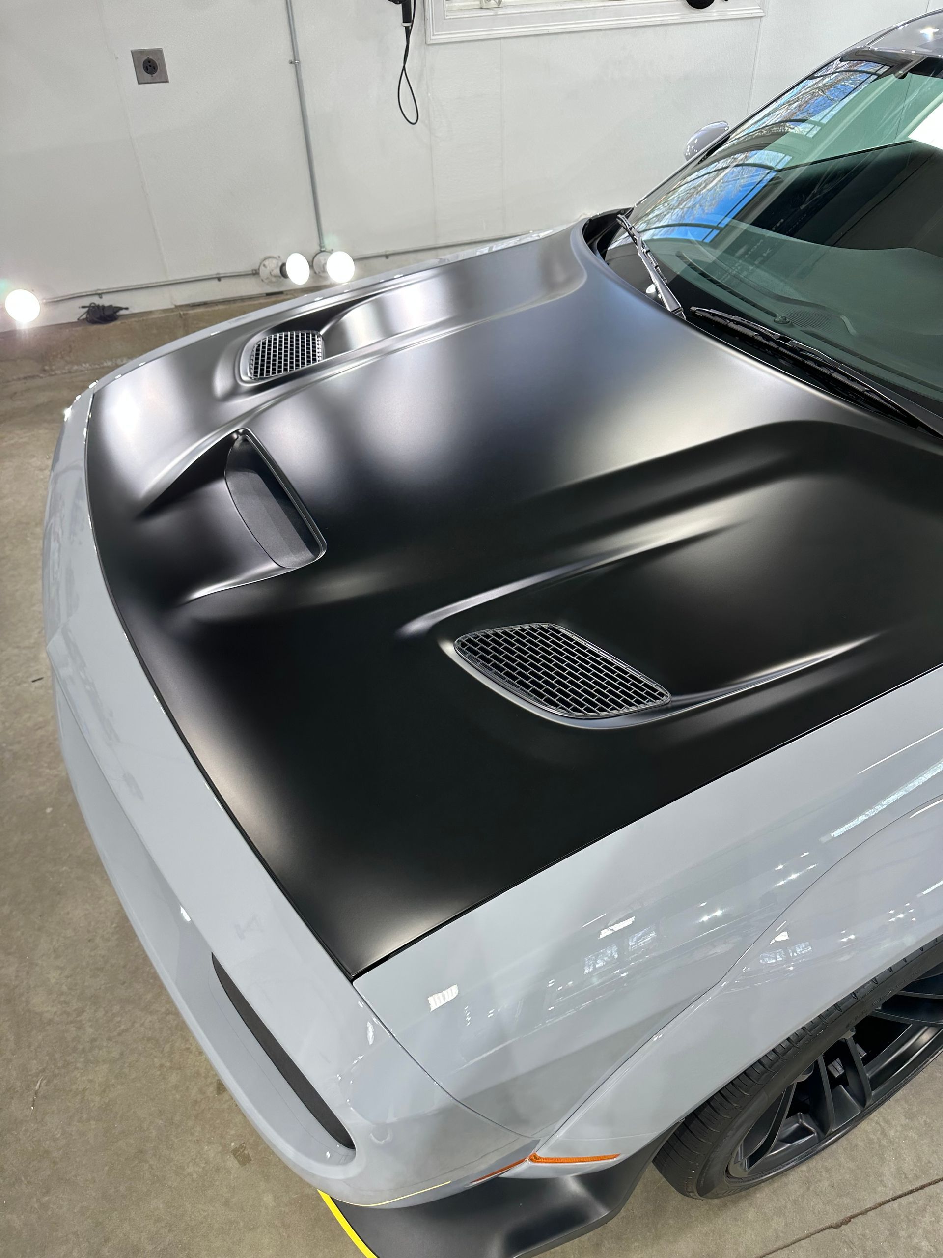 A white dodge challenger with a black hood is parked in a garage.