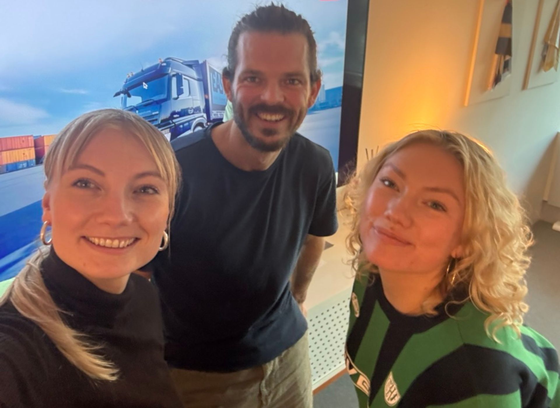 Een man en twee vrouwen poseren voor een foto voor een vrachtwagen.