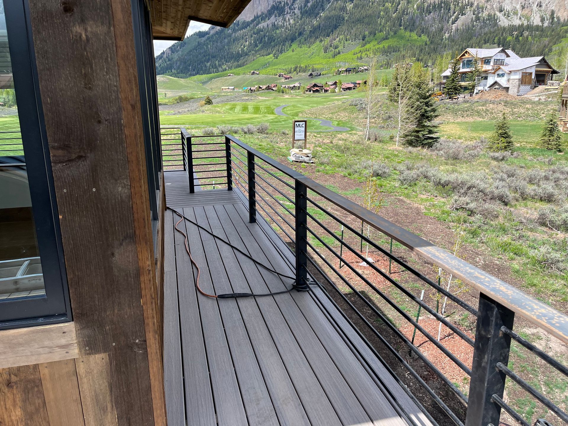 A wooden deck with a metal railing and a view of a mountain valley.