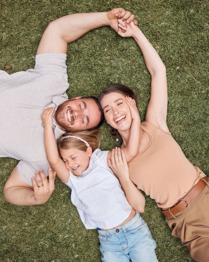 A family is laying on the grass making a heart shape with their hands.