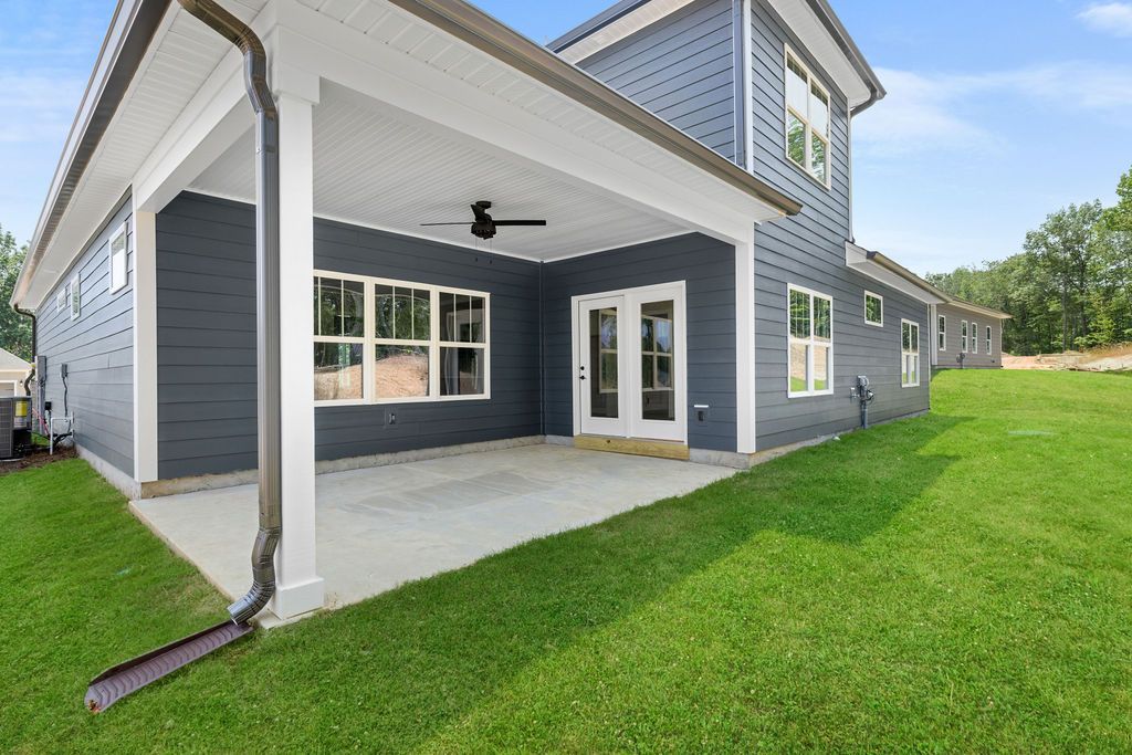 The back of a house with a covered patio and a large lawn.
