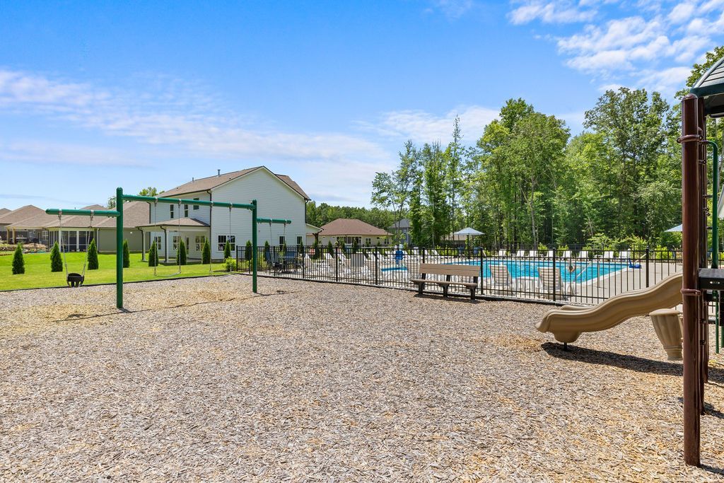A playground with swings , a slide , and a pool in the background.
