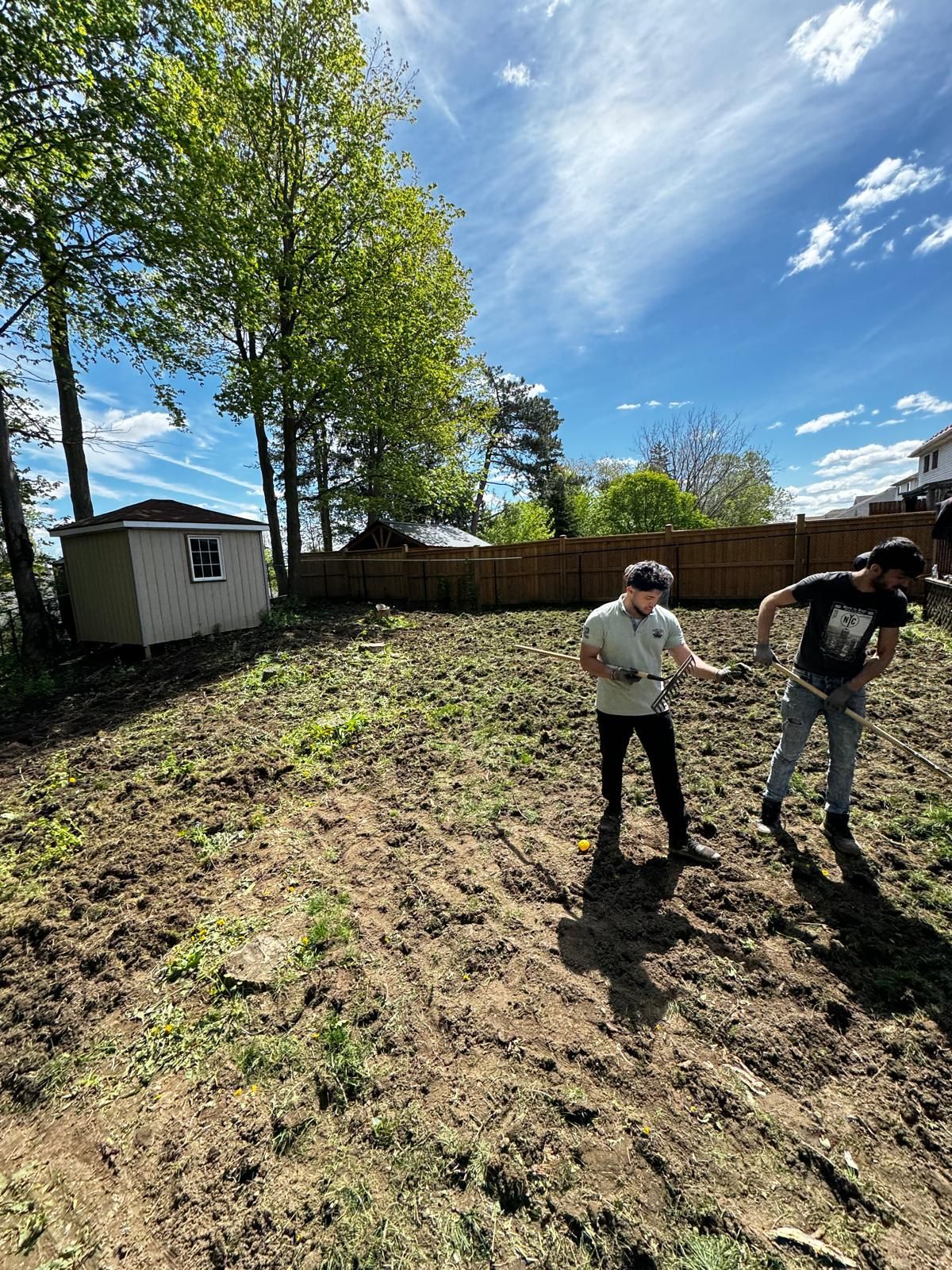 Two men are digging in a dirt field in a backyard.