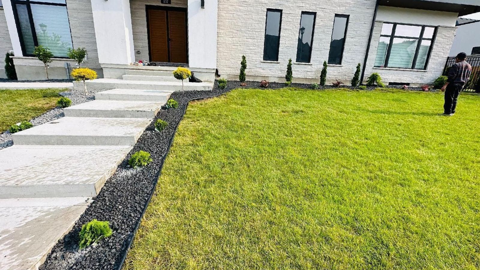 A man is standing in front of a house with a lush green lawn.