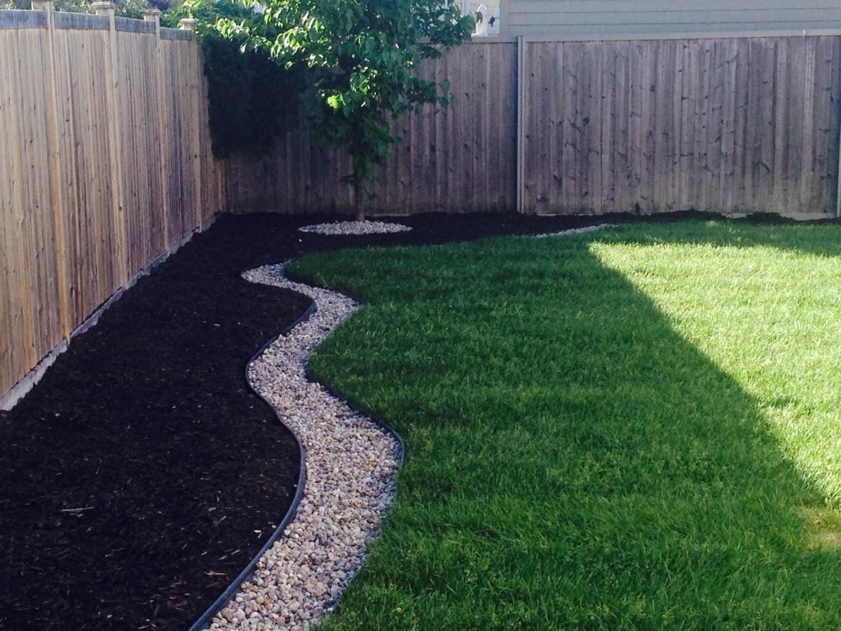 Backyard with a wavy gravel path separating dark mulch from green lawn, tree in center.