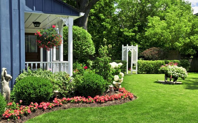 A blue house with a white porch and a lush green yard.