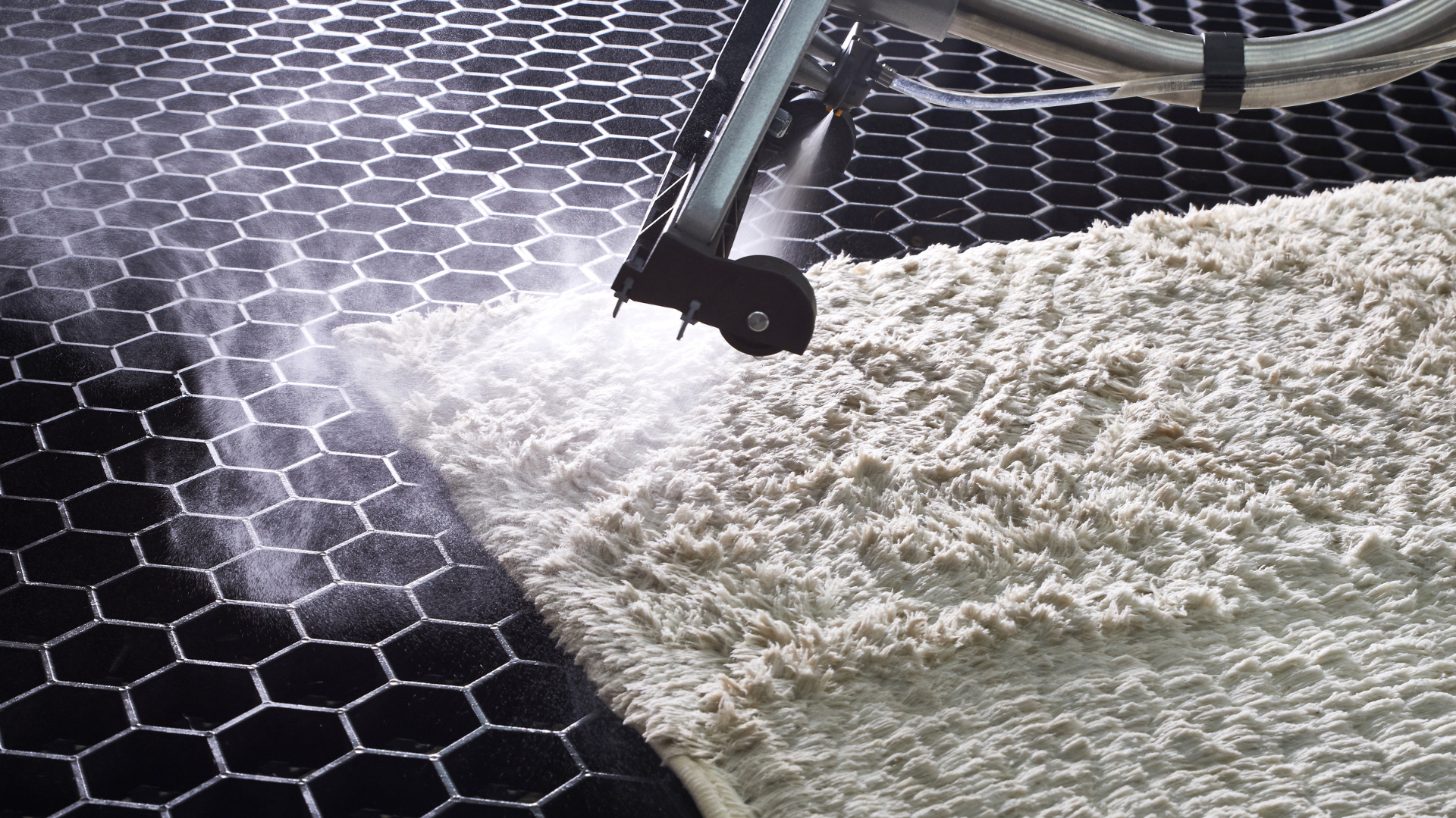 A vacuum cleaner is cleaning a rug on a black tile floor.
