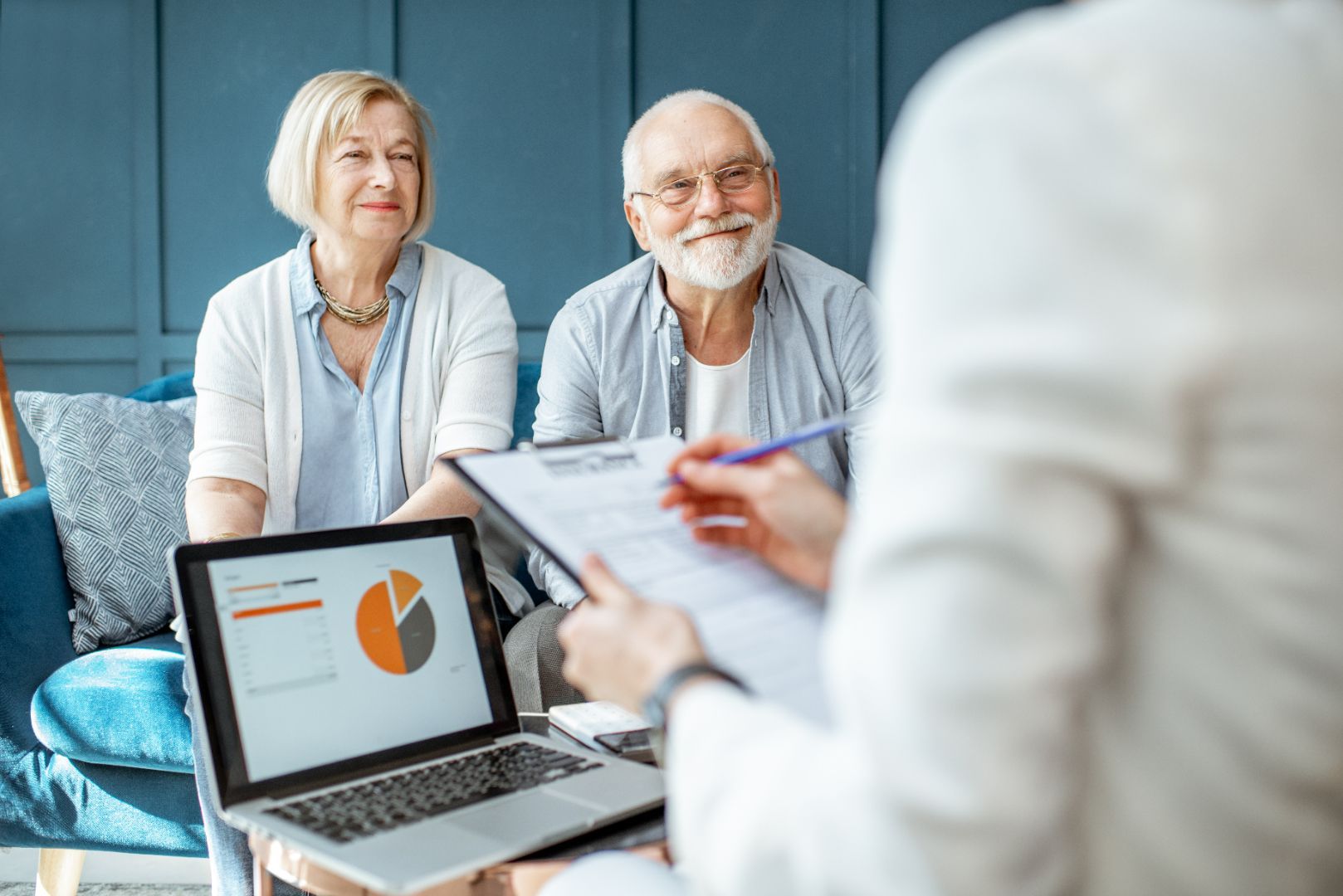 Senior couple smiling during a consultation with a financial advisor, who is showing them a laptop with a pie chart.