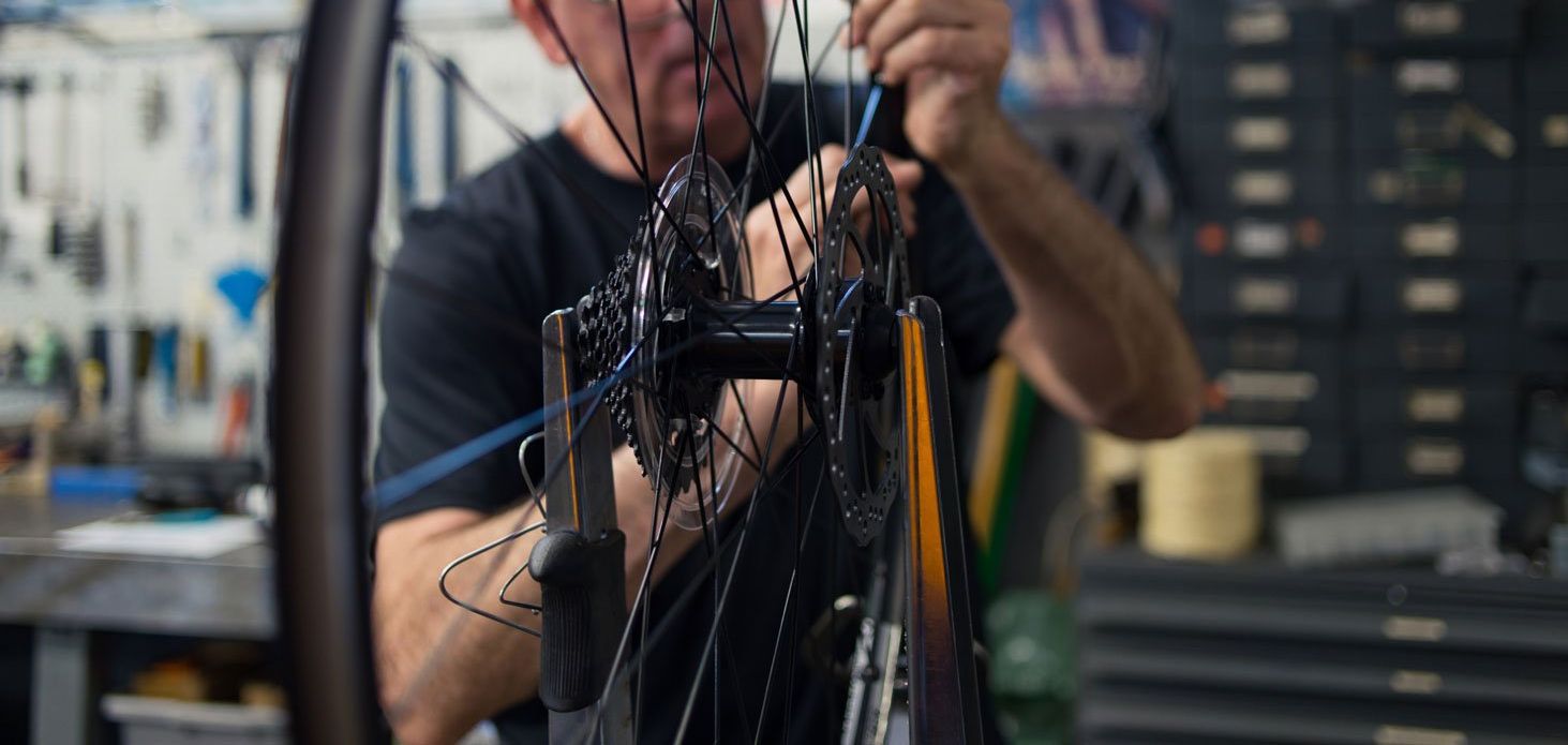 A man is working on a bicycle wheel in a workshop.