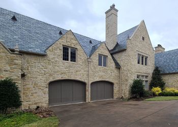 A large stone house with two garage doors and a chimney.