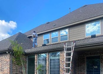 A man is standing on the roof of a house with a ladder.