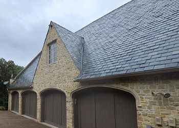 A large stone building with three garage doors and a slate roof.