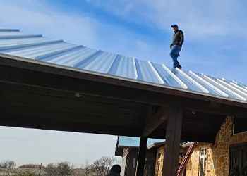 A man is standing on top of a metal roof.