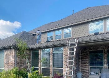 A man is standing on the roof of a house with a ladder.