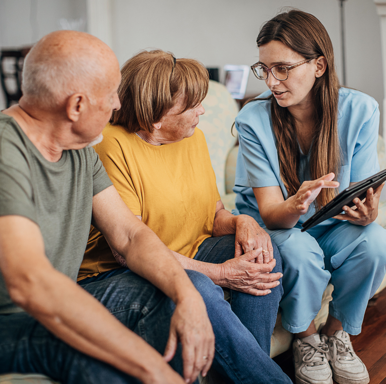 A group of people are sitting on a couch talking to a nurse who is holding a tablet.