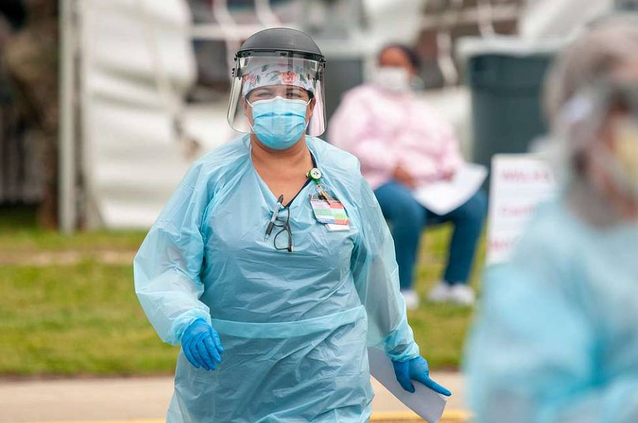 A nurse wearing a mask and a face shield is walking down the street.
