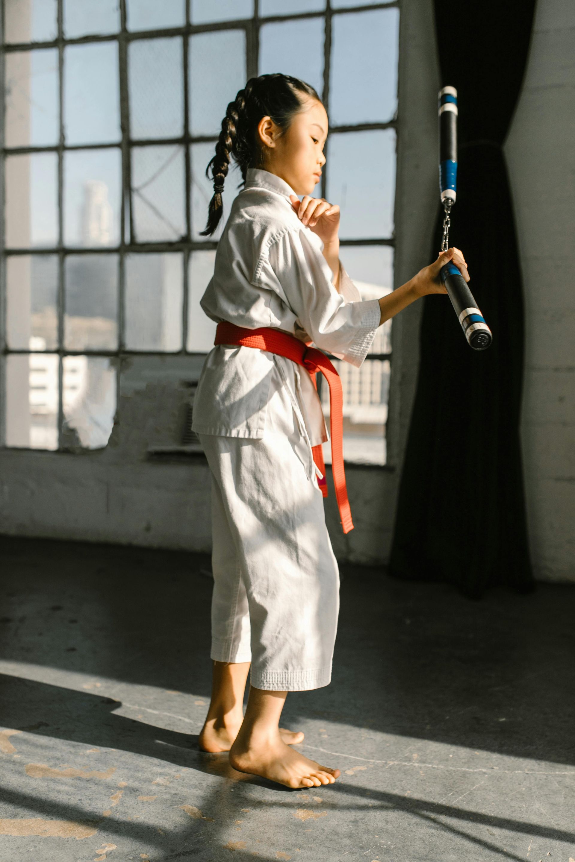 A young girl in a karate uniform is holding a bat.