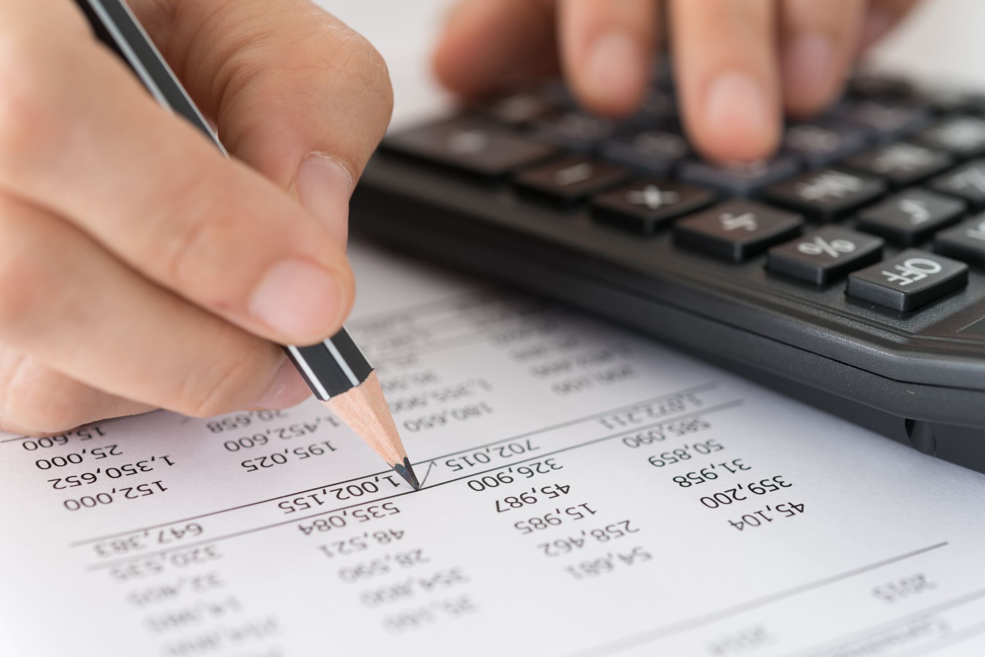 Hand holding pencil writing on a financial document beside a calculator