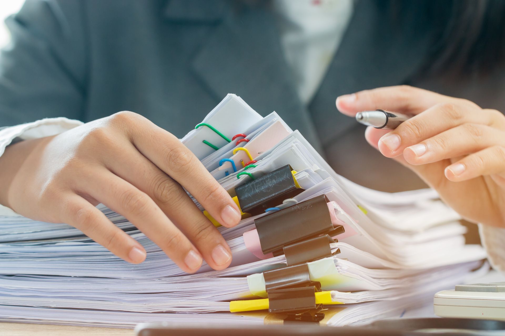 Hands sorting a stack of papers and colorful folders on a desk