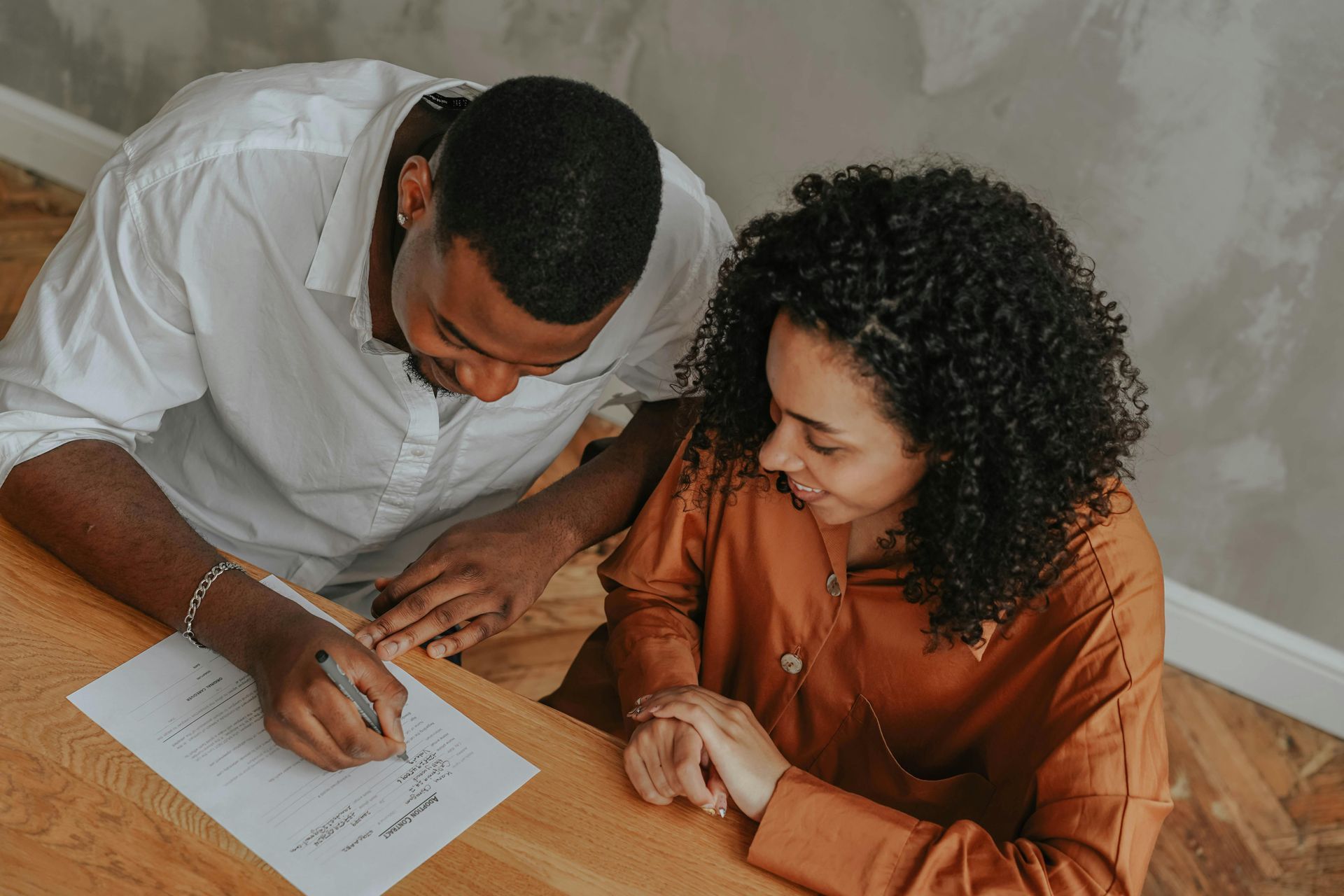 Two people reviewing a document together at a table, one writing with a pen.