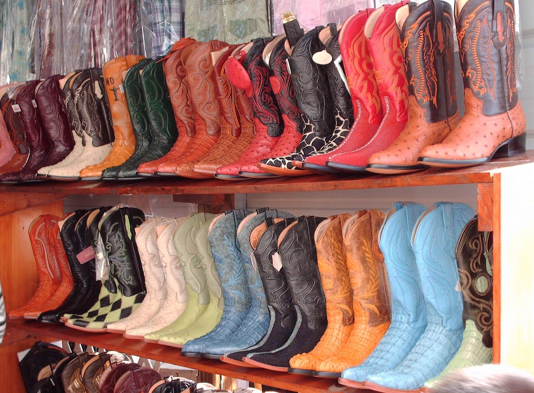 Rows of colorful cowboy boots on wooden shelves.