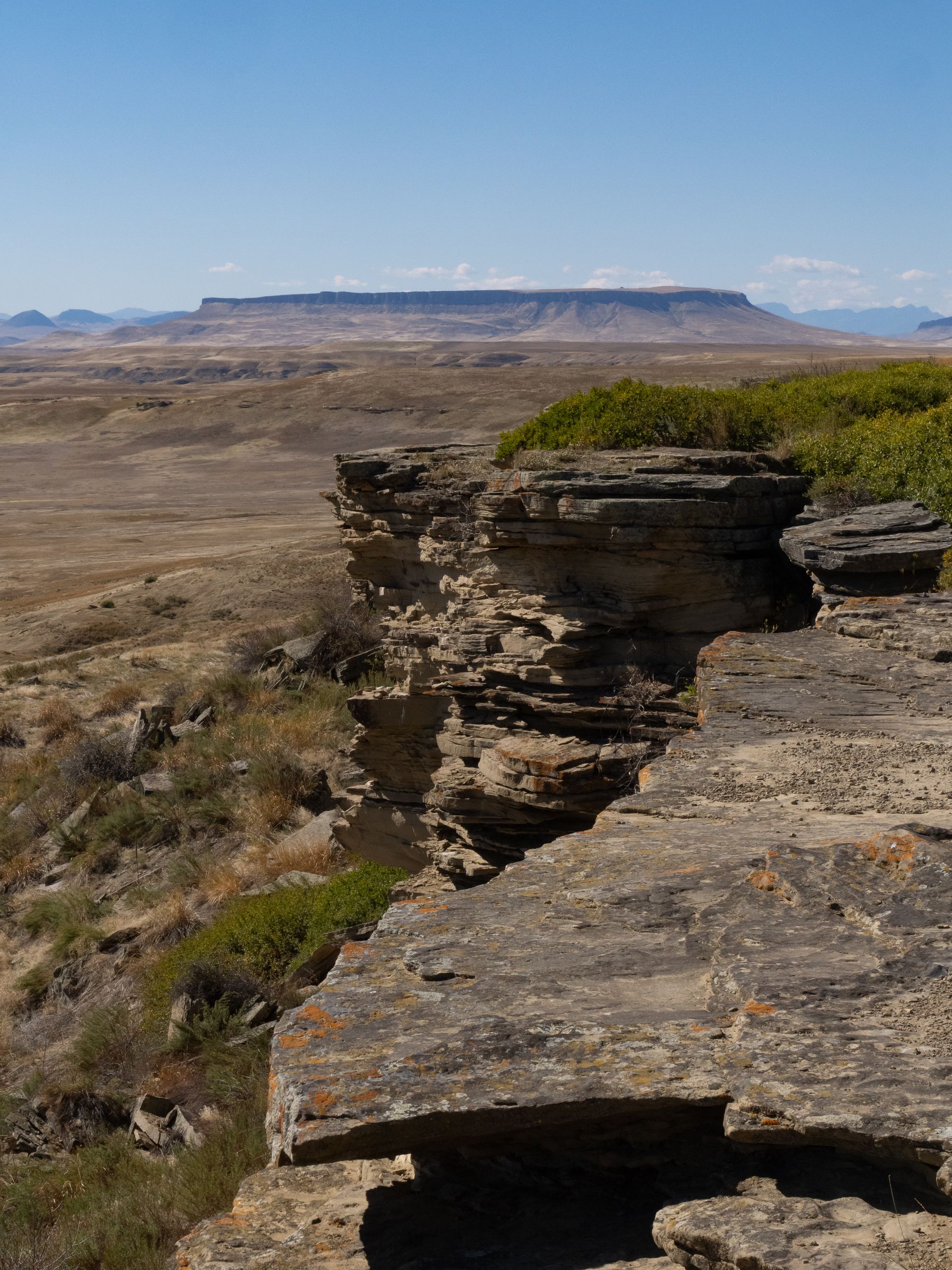 A view from a rocky cliff edge overlooking an arid desert landscape with a flat-topped mountain on the horizon.