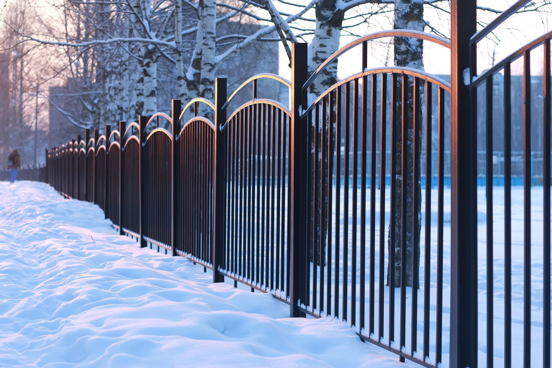 A wooden fence with a gate in the snow surrounded by snow covered trees.