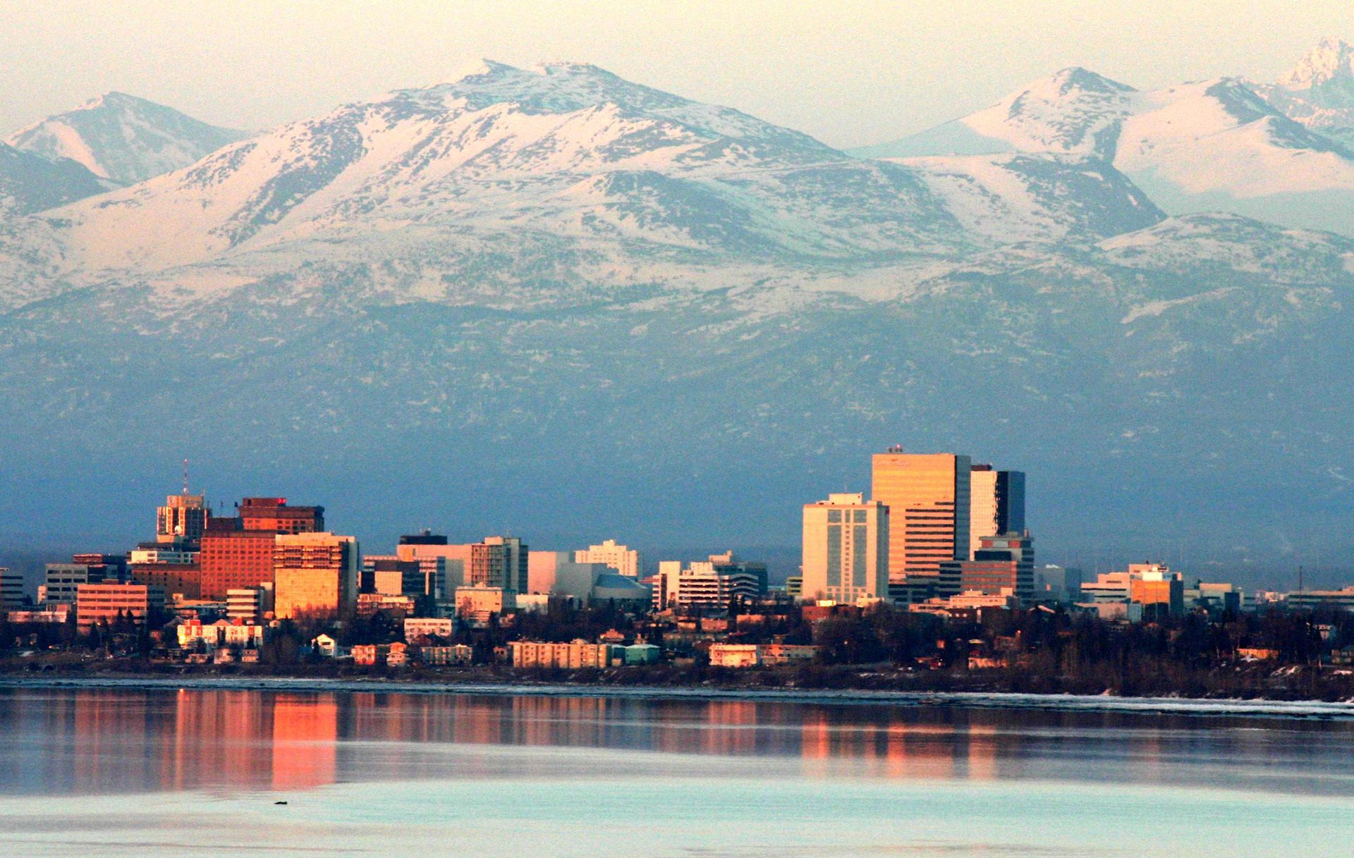 Anchorage, Alaska skyline with snow-capped mountains in the background and water in the foreground.