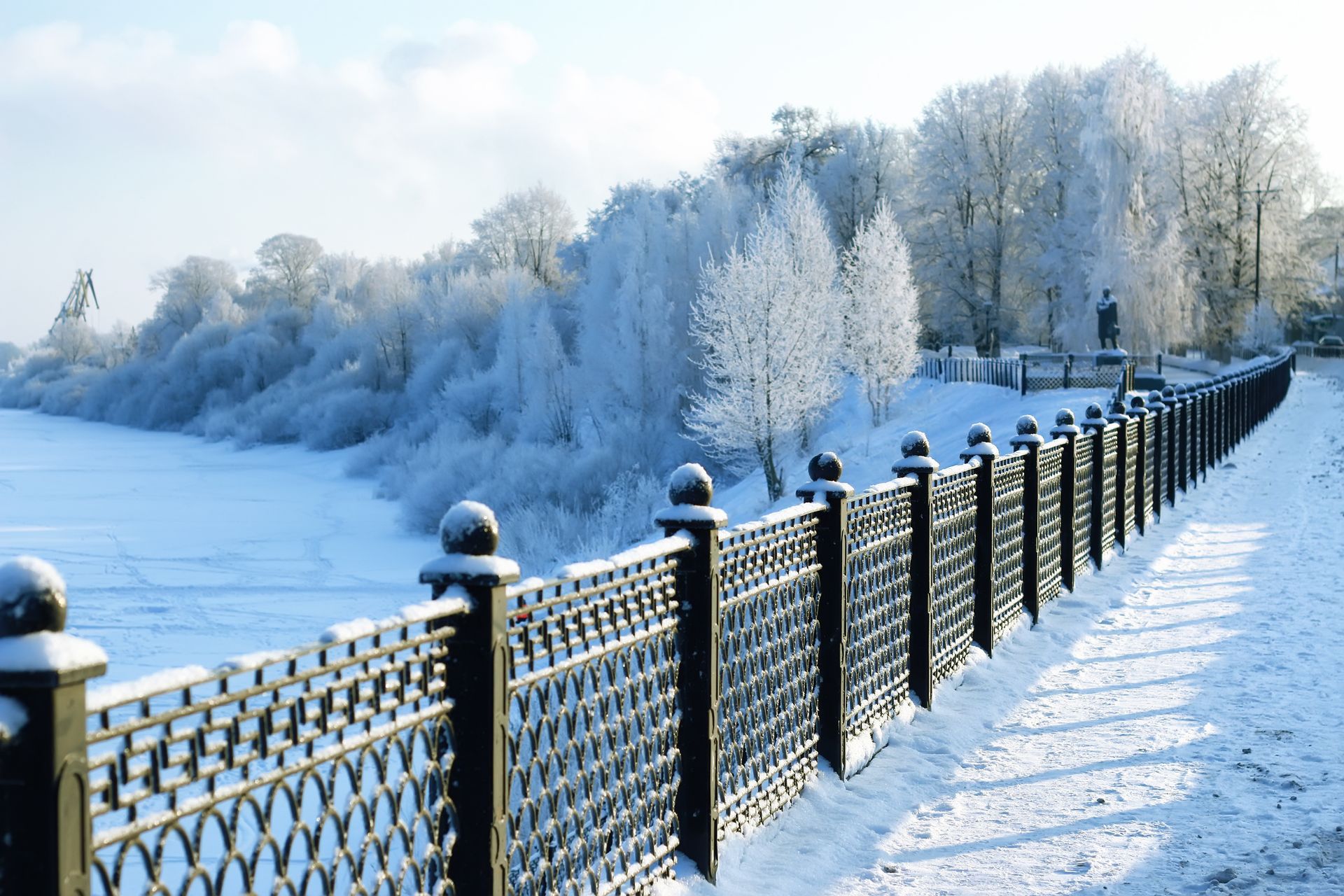 A snowy fence along a river with trees covered in snow in the background.