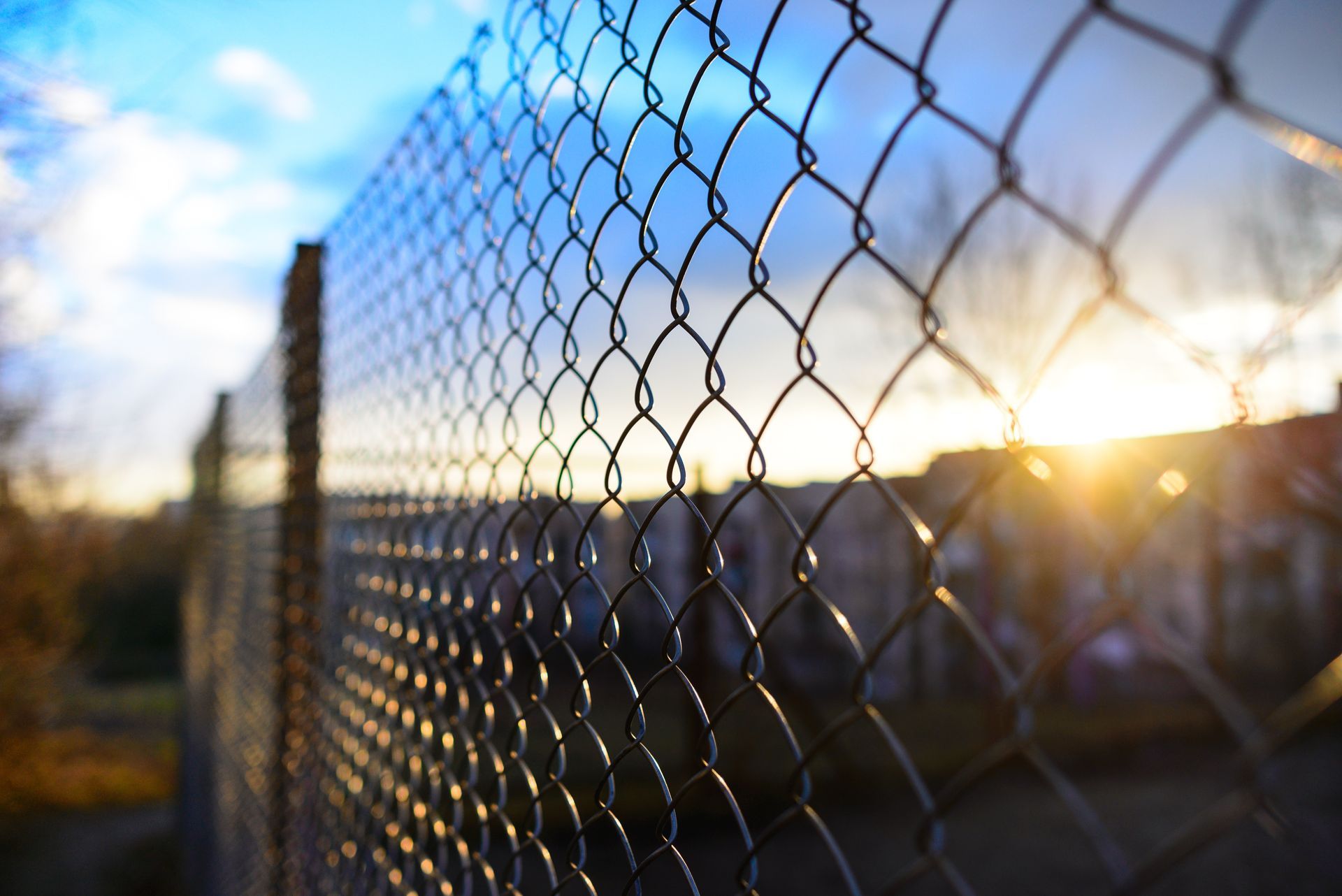 A close up of a chain link fence with the sun shining through it.