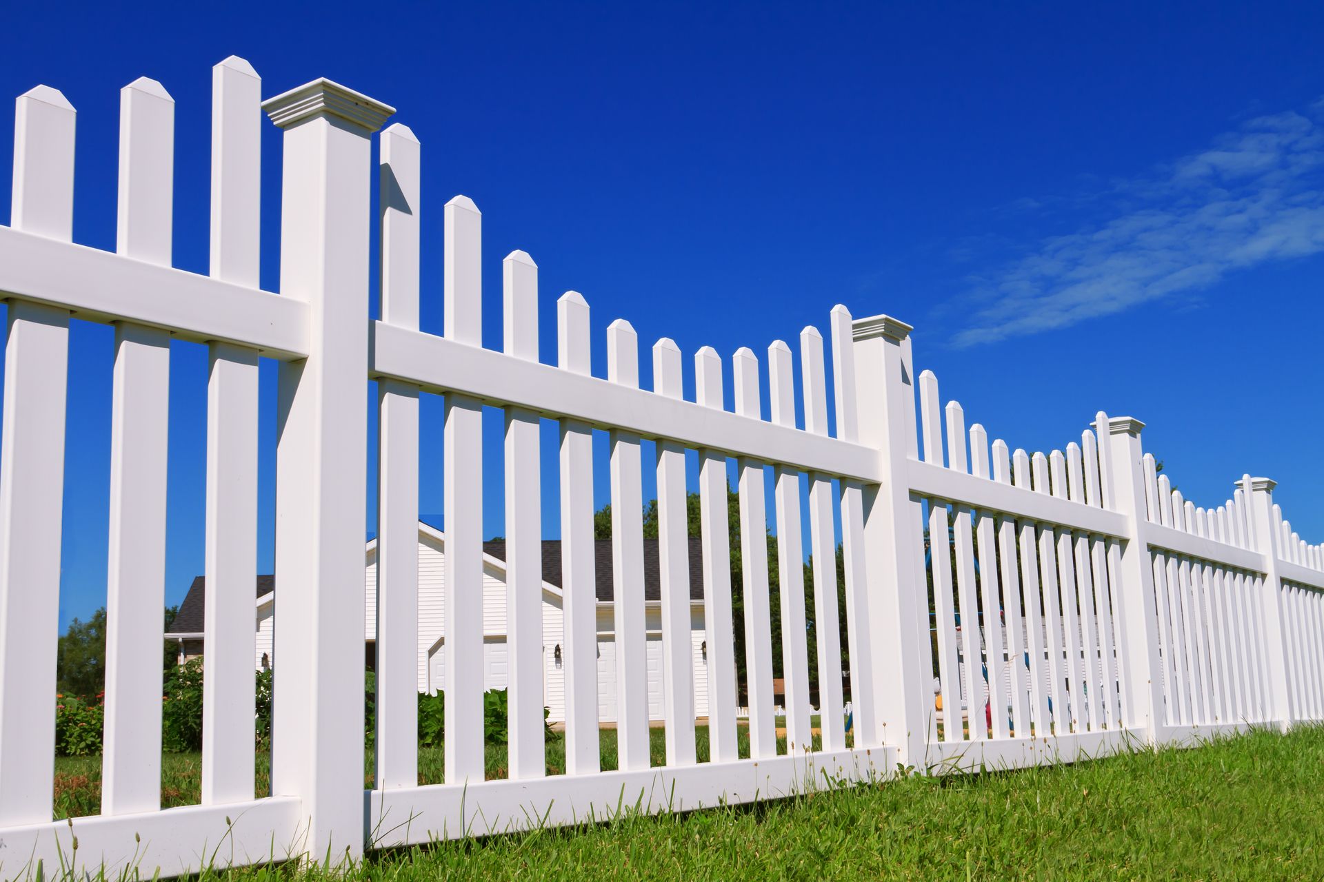 A white lattice fence is surrounded by snow in front of a house.