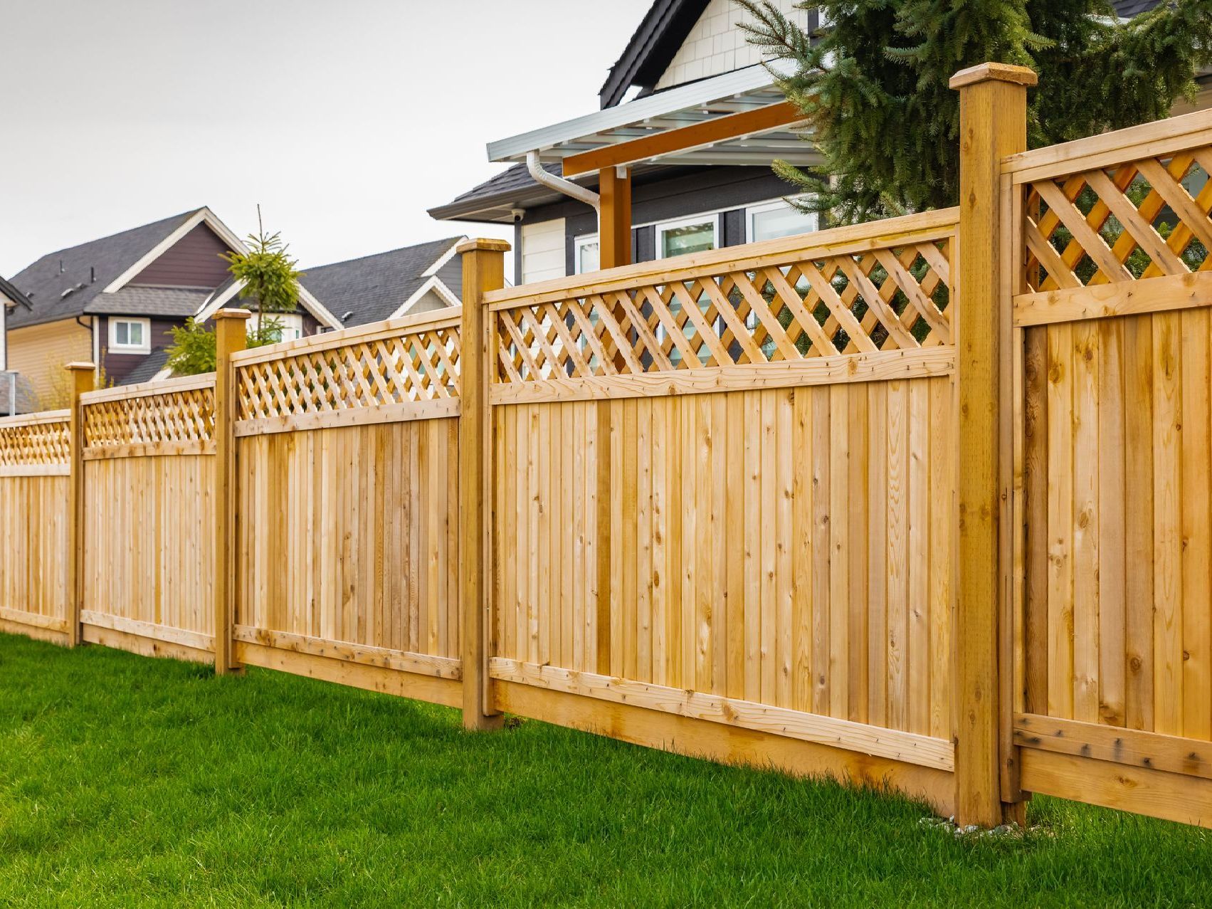 A wooden fence surrounds a lush green lawn in front of a house.