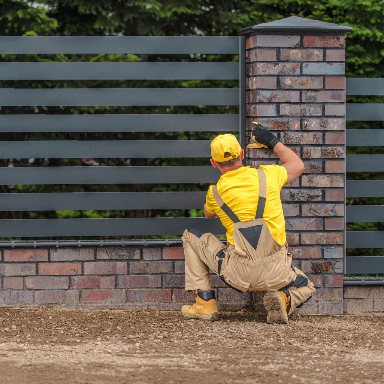 A man wearing a hard hat is working on a fence.