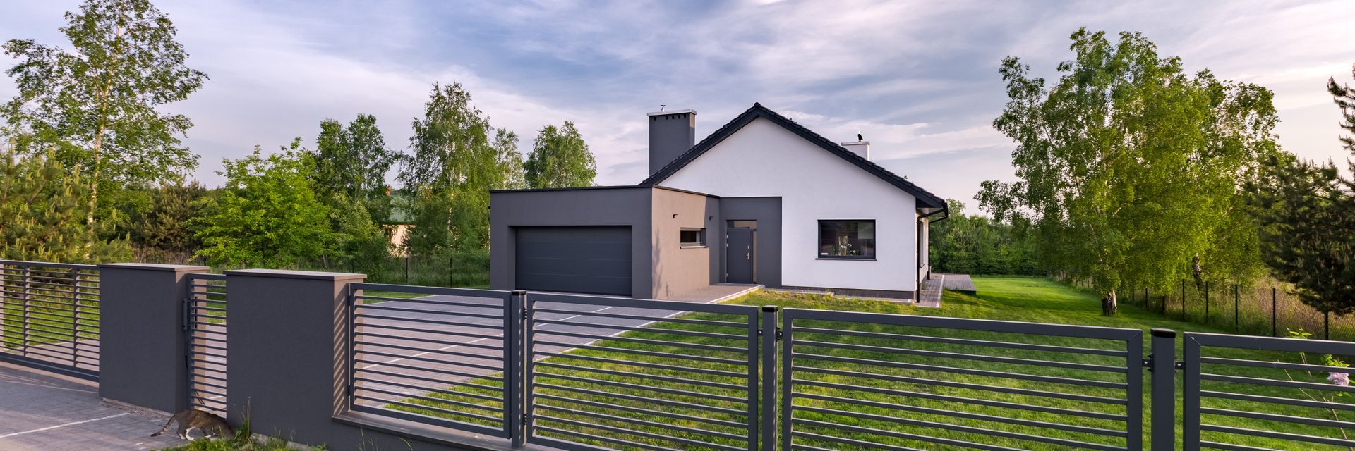 A white house with a black fence in front of it surrounded by trees.
