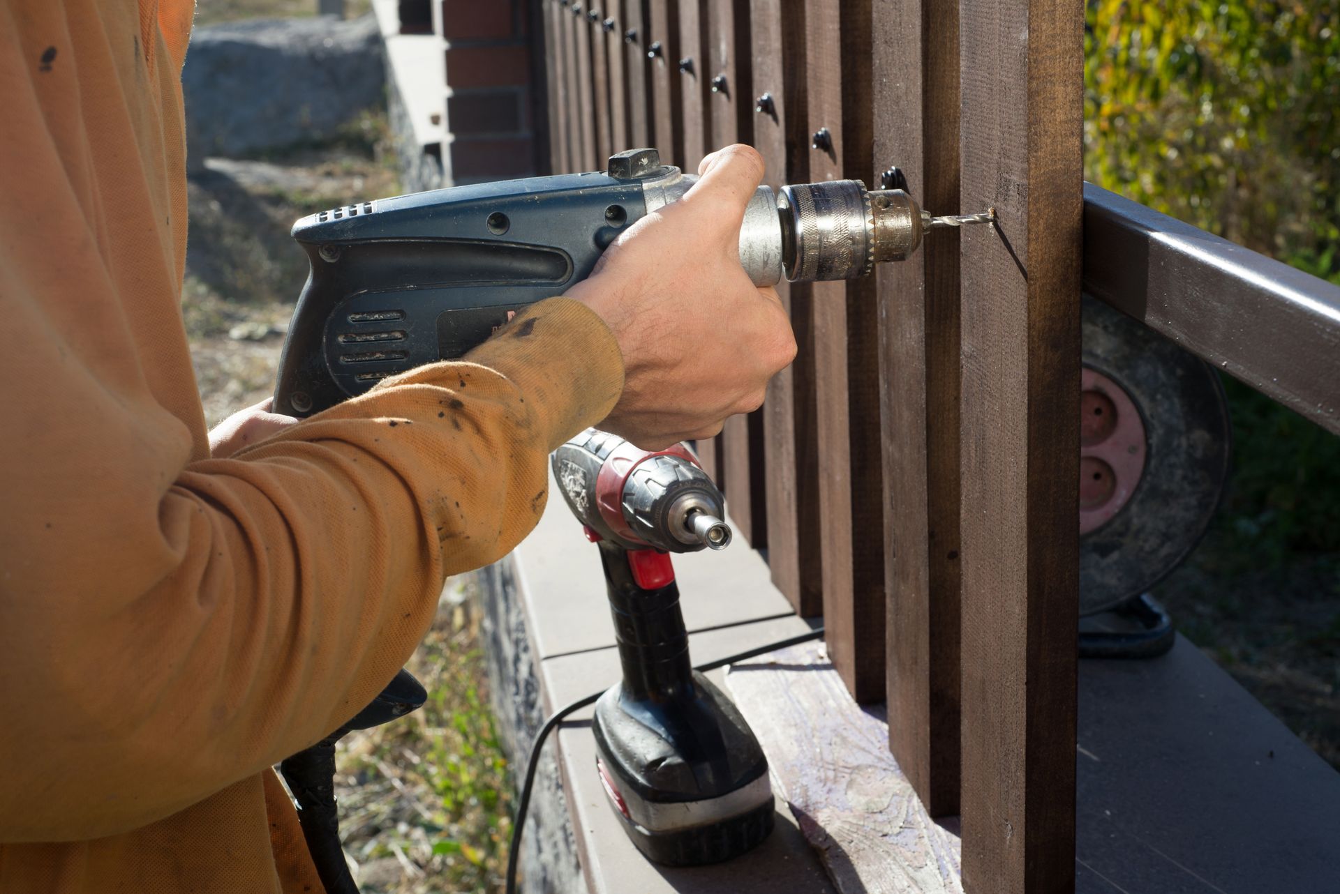 Person drilling a wooden fence with a power drill outside.