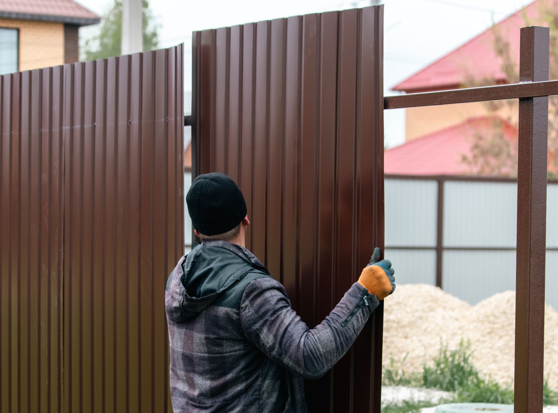 A man installing a brown corrugated metal gate in a residential area.