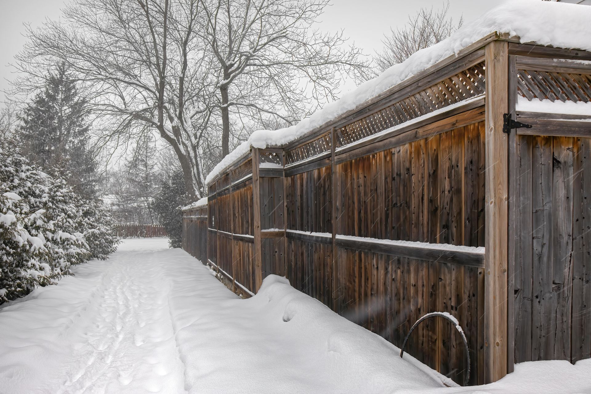 A wooden fence is covered in snow on a snowy day.
