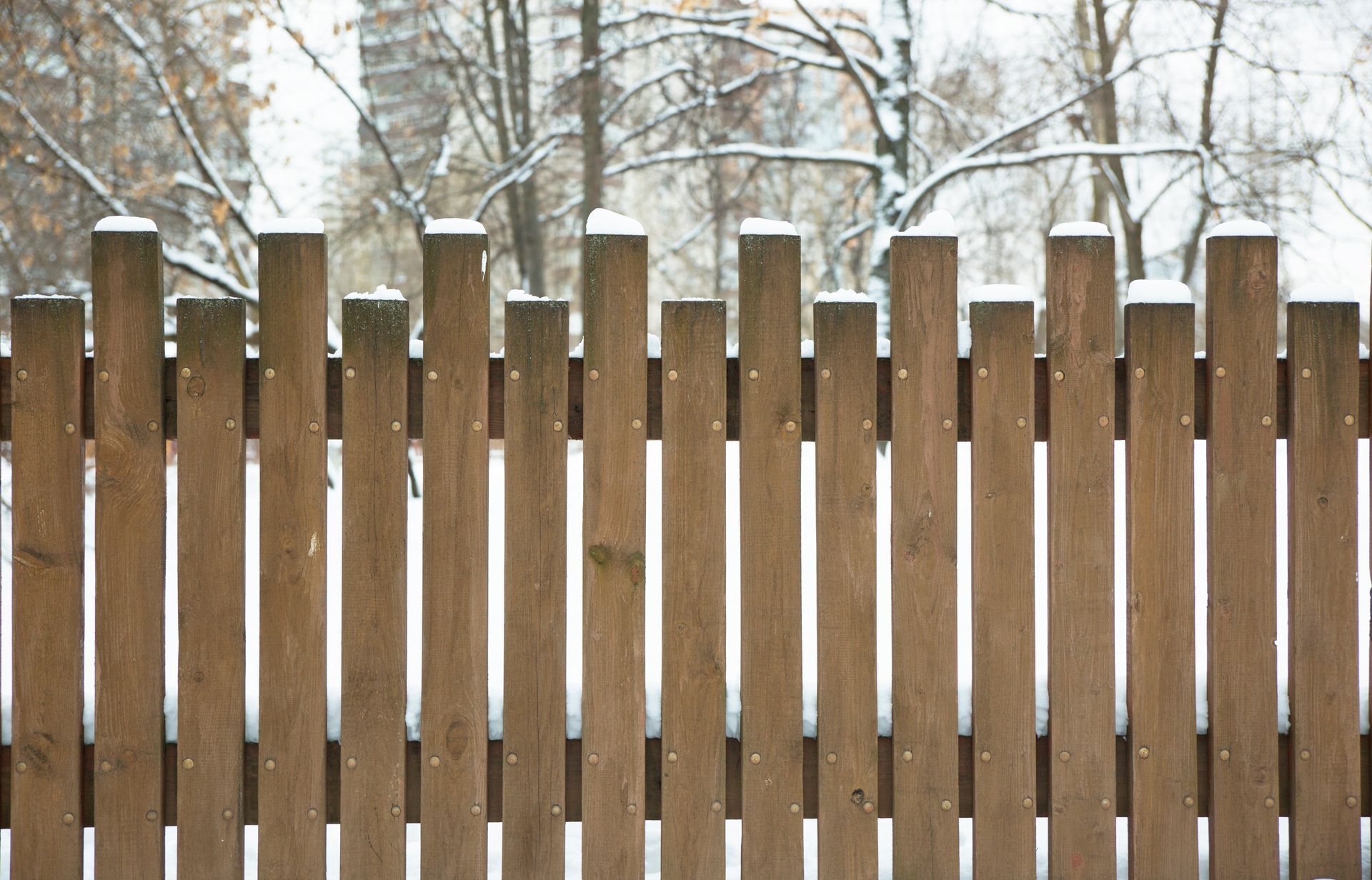 A white lattice fence is surrounded by snow in front of a house.