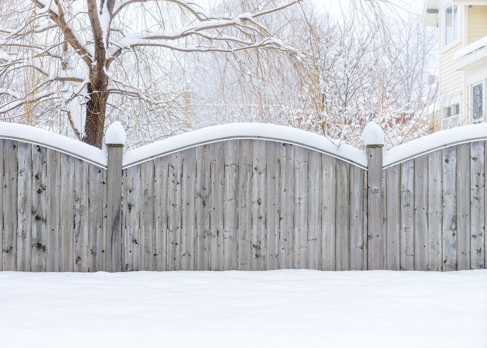 A wooden fence covered in snow with trees in the background.