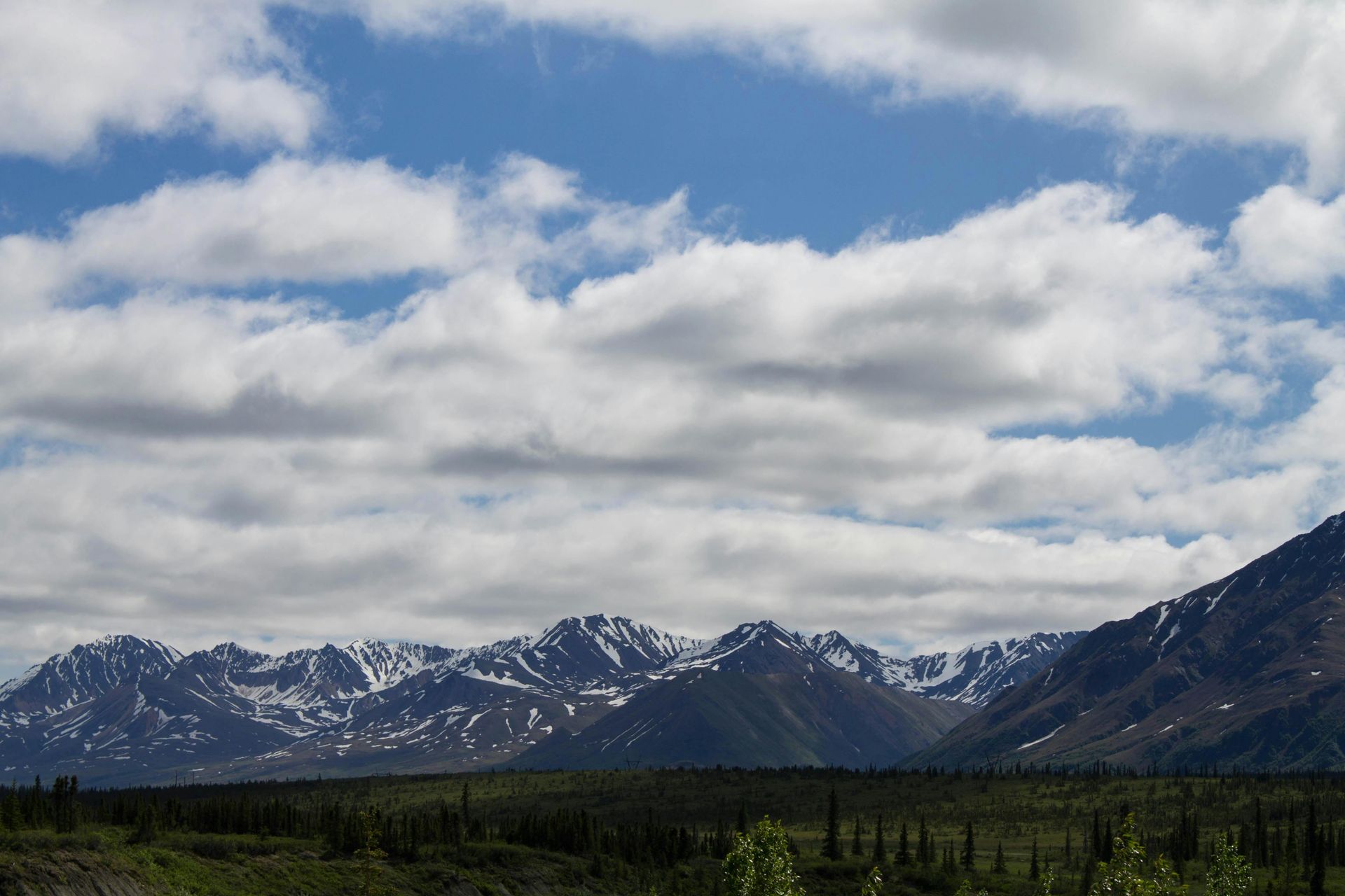 Mountains with snowy peaks under a cloudy blue sky. Lush green foreground.