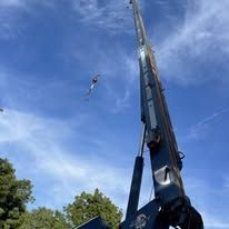 A tall, blue crane reaching into a bright blue sky. A kite is visible in the distance.