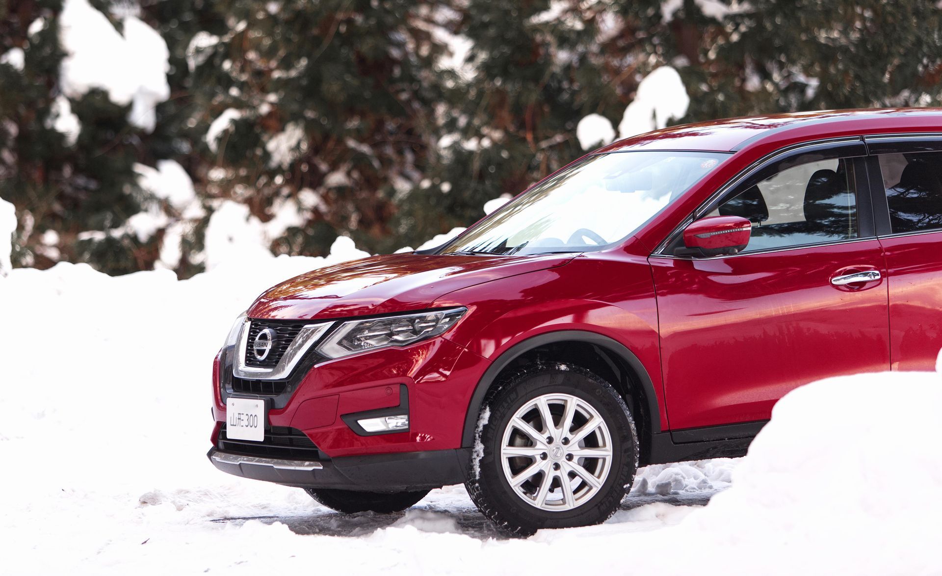 red nissan driving in the snow with snow tirs