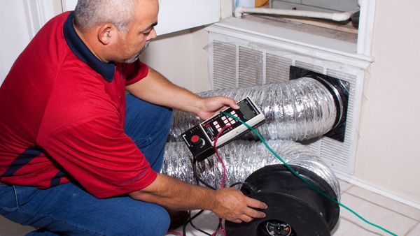 A man in a red shirt is kneeling down next to a fan and a hose.