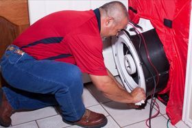 A man in a red shirt is kneeling down next to a fan.