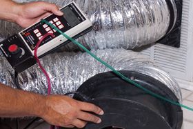 A person is using a thermometer to measure the temperature of a duct.