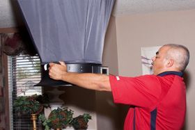 A man in a red shirt is working on a hood in a living room.