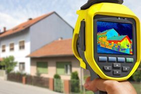 A person is holding a thermal camera in front of a house.