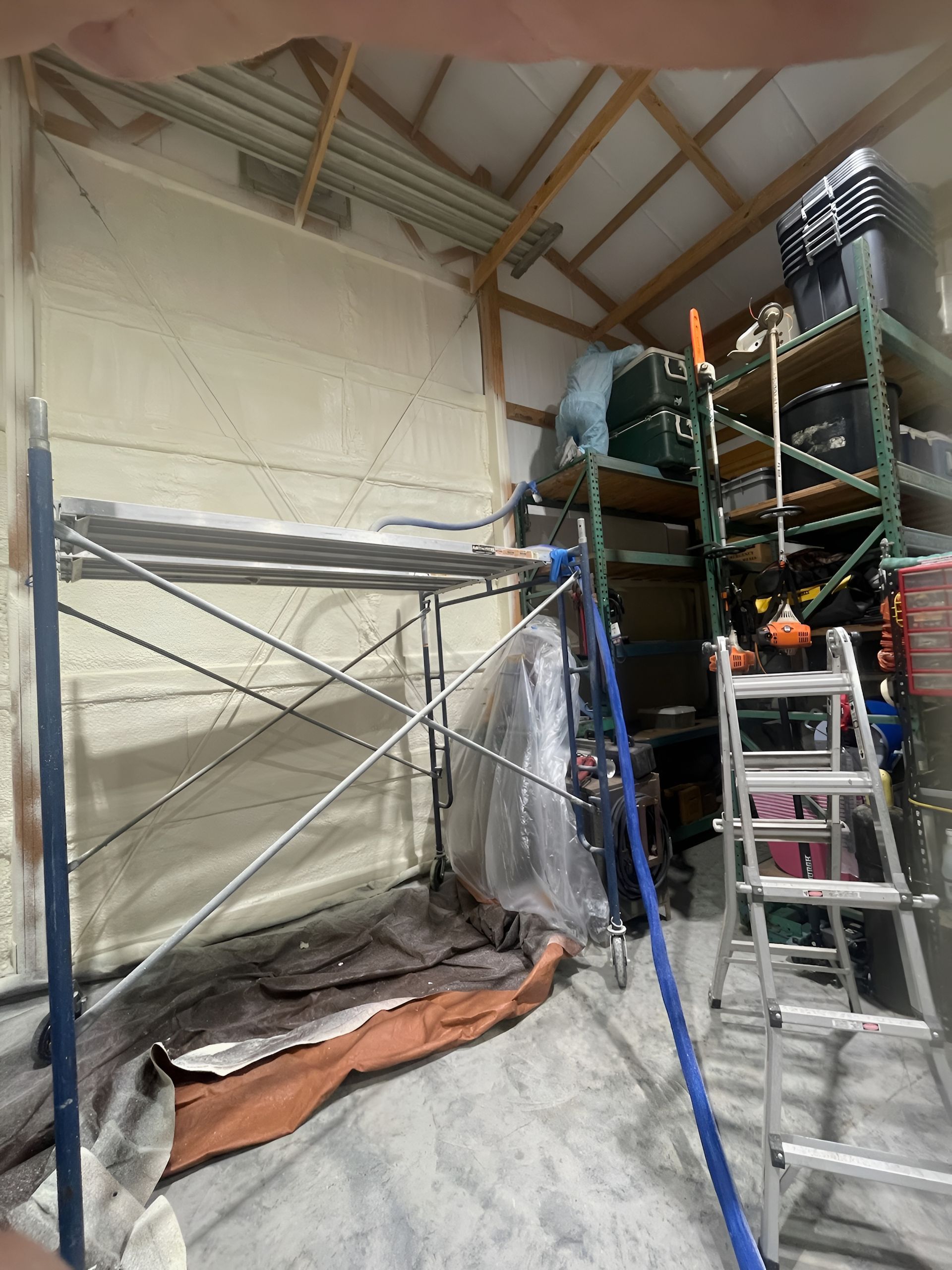 Interior view of a garage with scaffolding and spray foam insulation on the walls.