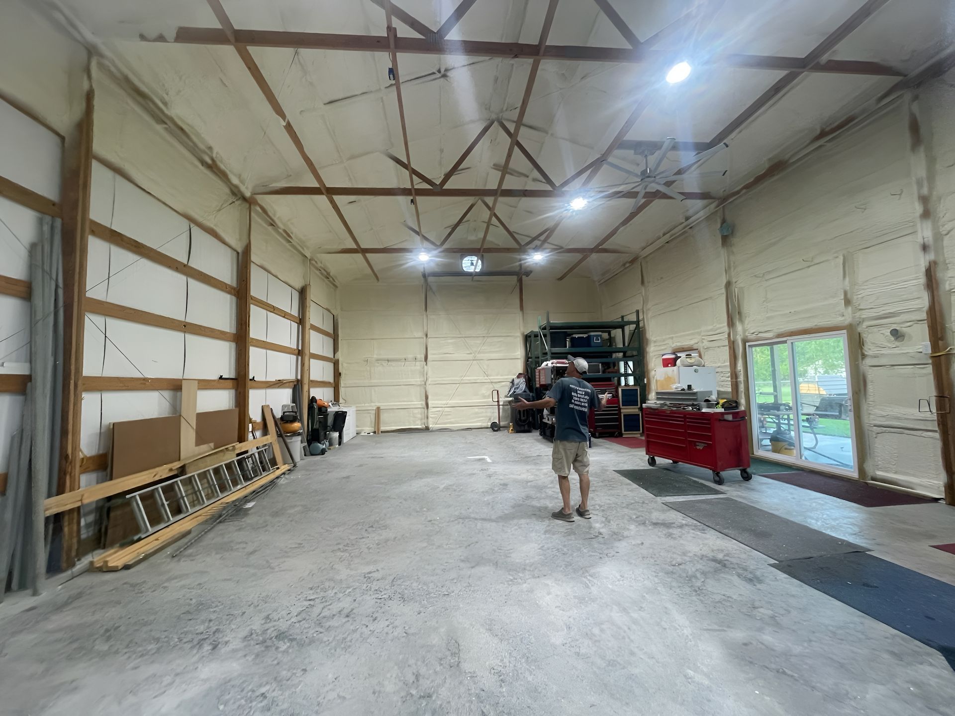 Interior of a spacious garage, with spray foam insulation and a person standing in the center.